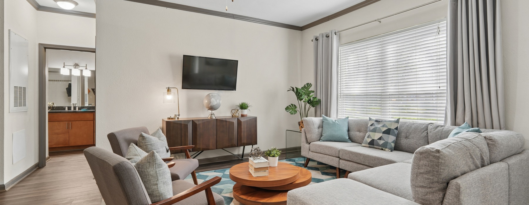 Presley Oaks apartment living room featuring open layout, ceiling fan, modern sectional seating, wood‑style flooring, and natural light